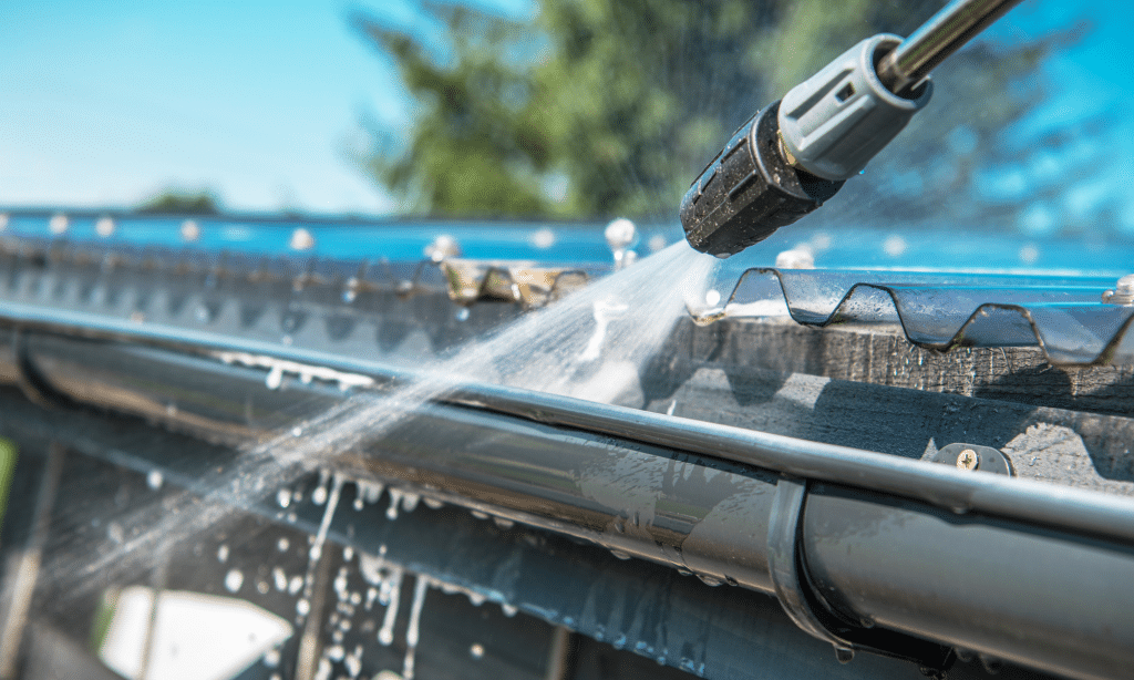 Close-up of a gutter being pressure washed, with water forcefully cleaning out debris