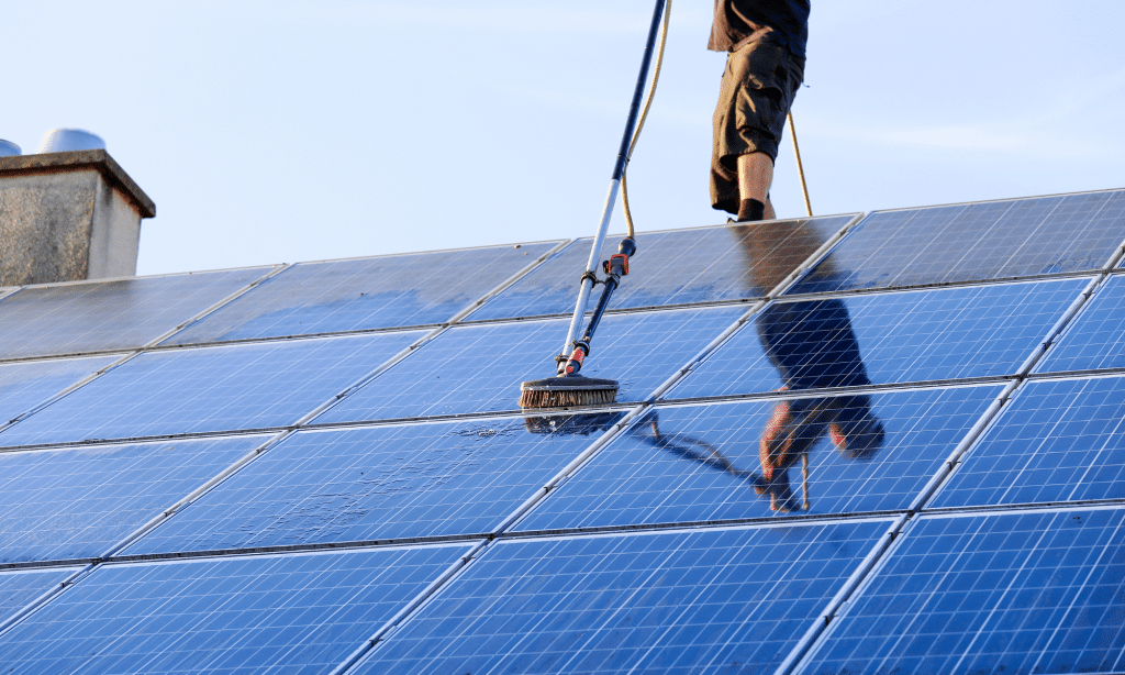 Person cleaning solar panels with a brush and water, emphasizing the importance of maintenance for energy efficiency